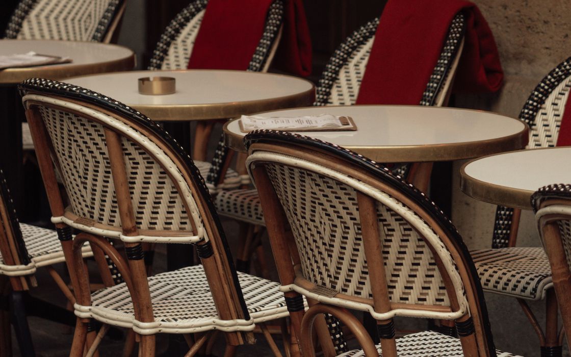 Woven bistro chairs with red blankets around small round caf&eacute; tables