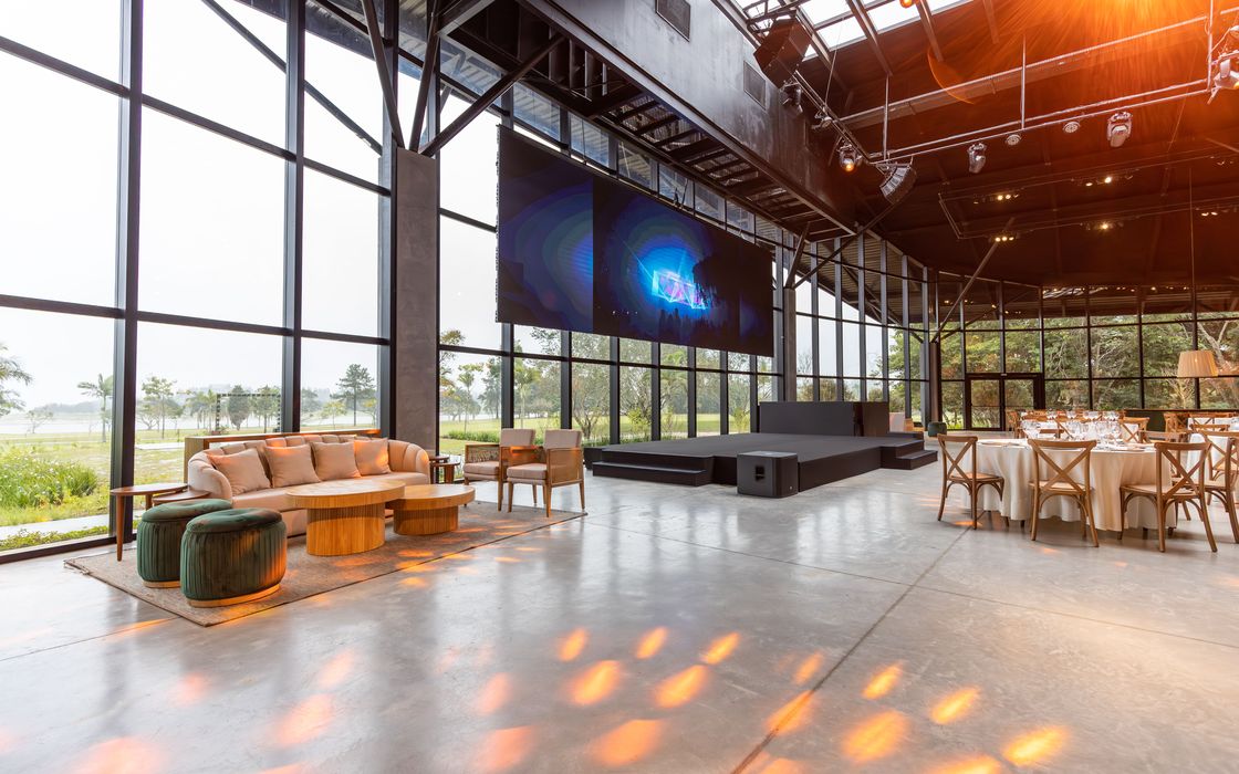 A glass-walled hall with a sofa corner, round tables and a lawn outside